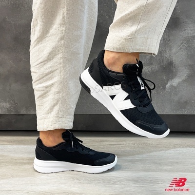Ténis New Balance pretos com detalhes brancos usados por pessoa com calças bege
