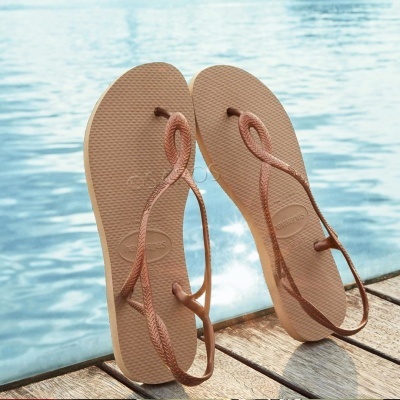 Chinelos de dedo bege com tiras rosa num deque junto à piscina