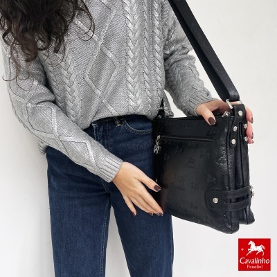 Pessoa segura mala preta Cavalinho com camisola cinzenta e jeans.