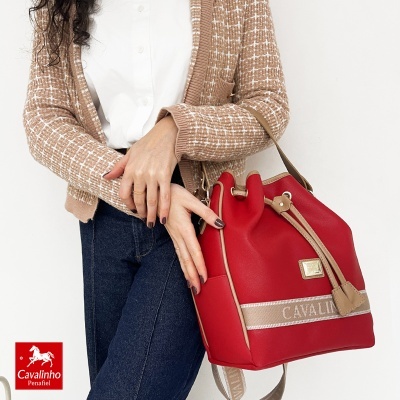 Mala vermelha com detalhes castanhos e texto CAVALINHO segurada por pessoa com camisola bege e jeans.