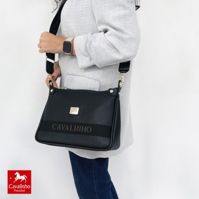 Mala preta Cavalinho com alça larga usada por pessoa com casaco cinzento