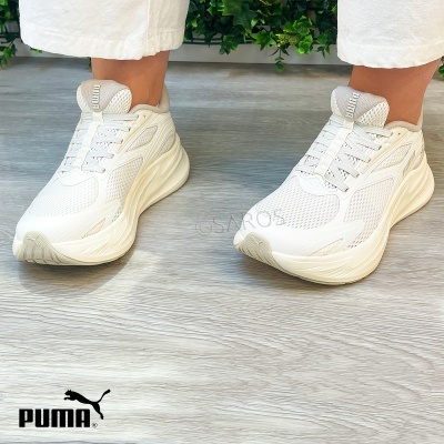 Sapatilhas desportivas brancas Puma em piso de madeira com planta.