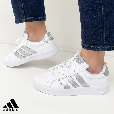 Ténis Adidas brancos com riscas prateadas e sola branca usados com calças de ganga