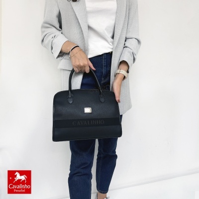 Mulher com mala preta Cavalinho, blazer cinzento, t-shirt branca e jeans azul escuro