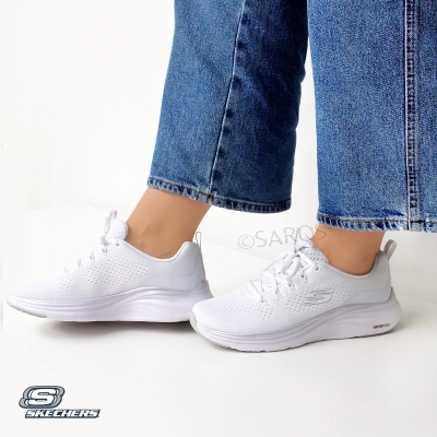 Tênis desportivo Skechers brancos em fundo branco com calças de ganga azuis