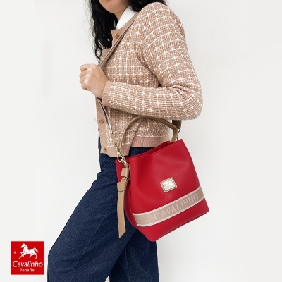 Mala vermelha Cavalinho com tira bege e faixa personalizada, usada por pessoa com cardigan bege e calças de ganga