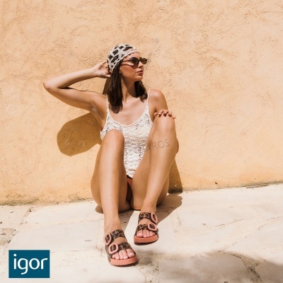 Mulher com fato de banho branco de crochet e sandálias com padrão leopardo sentada junto a parede bege