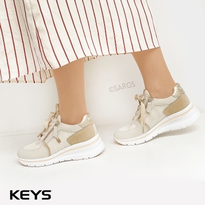 Ténis femininos bege e branco com sola alta e detalhes em tecido e couro, usados com saia às riscas vermelhas.