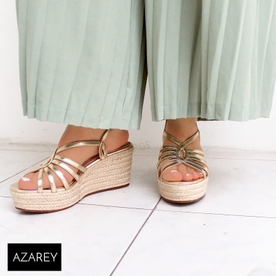 Sandálias de cunha douradas Azarey usadas com calças verdes claras no chão branco.