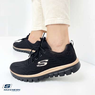 Ténis Skechers pretos com sola preta e detalhes dourados usados com calças bege