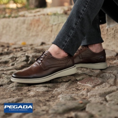 Sapatos castanhos de cabedal com atacadores e sola branca em pavimento de pedra.