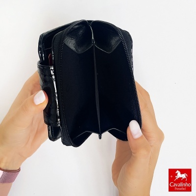 Carteira preta em pele com fecho, interior aberto, mãos femininas segurando