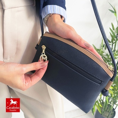 Bolsa preta e castanha com zipper dourado segurada por pessoa com roupa azul e creme em ambiente interior