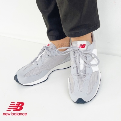Ténis New Balance cinza com detalhes brancos e logo vermelho, calçado em pés com calças pretas, fundo branco