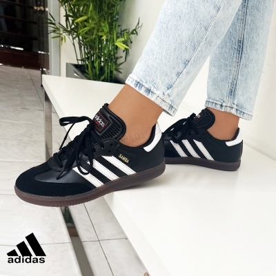 Ténis Adidas Samba pretos com riscas brancas usados em ambiente interior