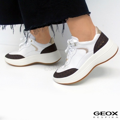 Ténis brancos com detalhes castanhos escuros e dourados, sola branca alta, usados num fundo branco