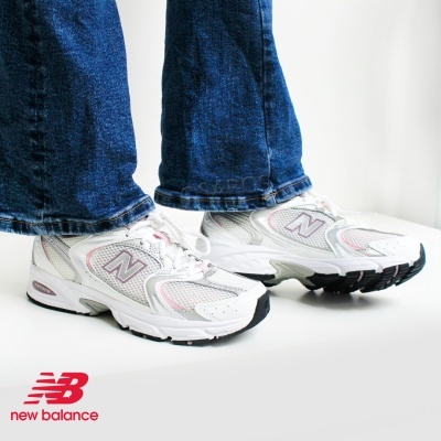 Sapatilhas New Balance brancas com detalhes cinza e rosa e sola preta, usadas com jeans azuis