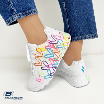 Ténis brancos Skechers com corações coloridos usados com jeans azuis