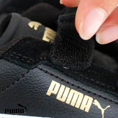 Tênis preto Puma com logótipo dourado e aba de velcro sendo segurada por mão