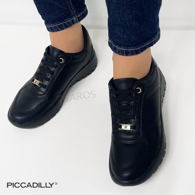 Ténis pretos de pele com sola preta e detalhes dourados, usados com calças de ganga