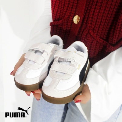 Sapatilhas brancas Puma com faixa preta, sola castanha e fecho de velcro, seguradas por pessoa com colete vermelho.