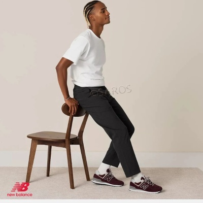 Homem sentado numa cadeira de madeira, veste roupa casual com sapatilhas New Balance bordô
