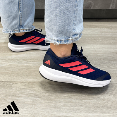 Ténis Adidas azul escuro com riscas cor-de-rosa e sola branca em fundo de chão de madeira.