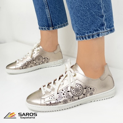 Ténis dourados com padrão floral recortado e sola branca usados com jeans azuis