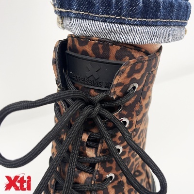 Bota padrão animal castanho e preto com atacadores pretos e etiqueta preta na língua com texto, usada com calças de ganga