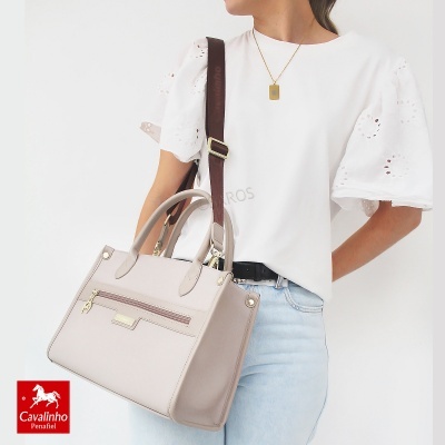 Mala de senhora bege claro com alças castanhas e bolso frontal, acompanhada de roupa casual branca e jeans