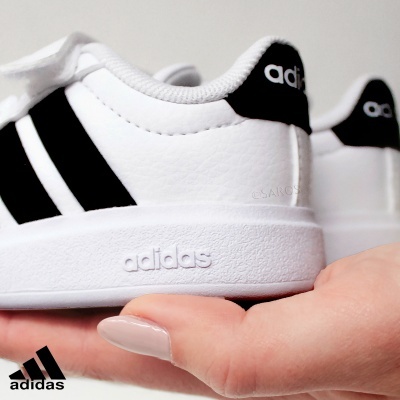 Sapatilhas Adidas brancas com riscas pretas e sola branca, seguradas por uma mão.