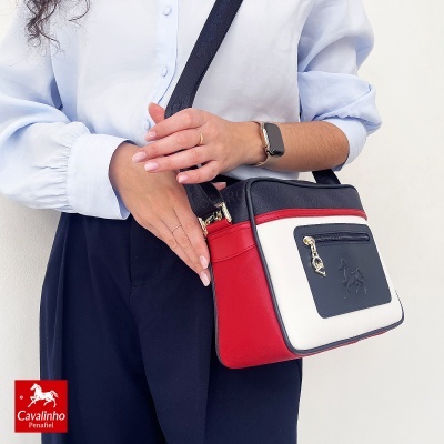 Mala transversal Cavalinho Penafiel preta, branca e vermelha com bolso frontal e pendente dourado.