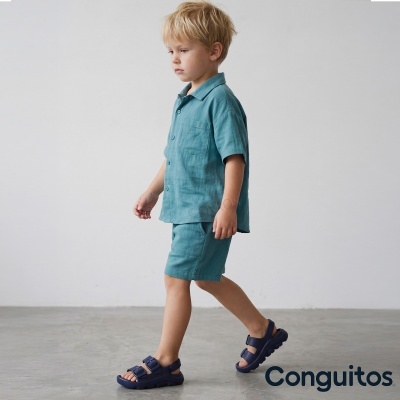 Criança loira a andar vestida com camisa e calções azuis e sandálias azuis