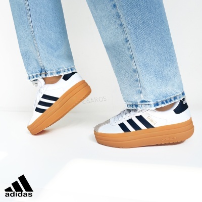 Ténis Adidas brancos com riscas pretas e sola castanha, usados com jeans azuis claros