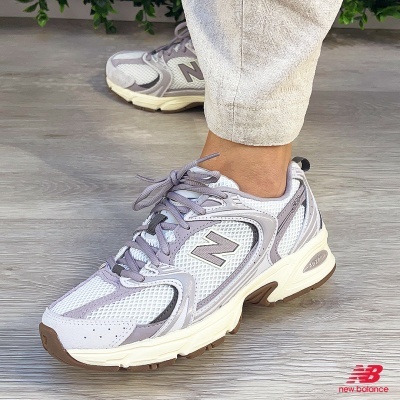 Ténis New Balance cinza e branco em pé com calças claras