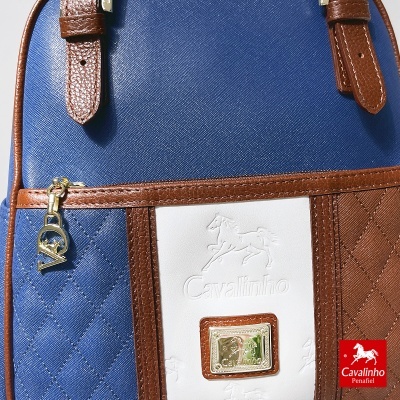 Mala azul com detalhes castanhos e emblema Cavalinho em branco com placa dourada.