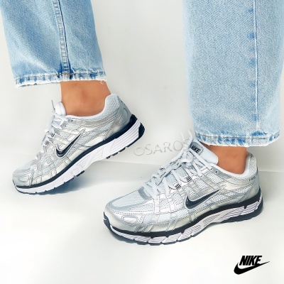 Ténis desportivos Nike prateados com logótipo preto usados com calças de ganga