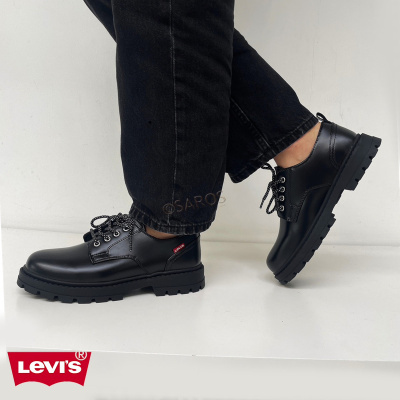 Sapatos pretos de couro Levis com sola grossa e atacadores, calçados por pessoa com calças pretas