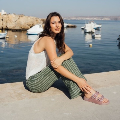 Mulher jovem com roupa casual sentada ao ar livre perto do mar com barcos ao fundo