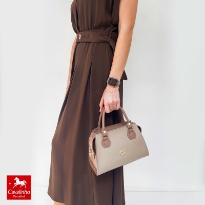 Pessoa a segurar mala castanha clara com detalhes castanhos e vestido castanho escuro