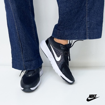 Ténis Nike pretos com sola branca e logo branco usados com calças de ganga azul escuro
