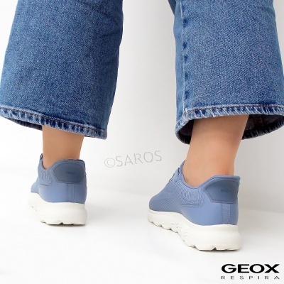 Ténis desportivos azuis com sola branca usados por pessoa com calças de ganga