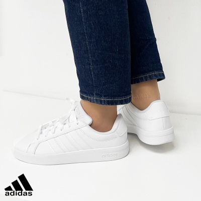 Ténis Adidas brancos com riscas características usados com jeans escuros