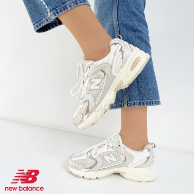 Ténis New Balance brancos e cinzentos com sola grossa usados com jeans azul