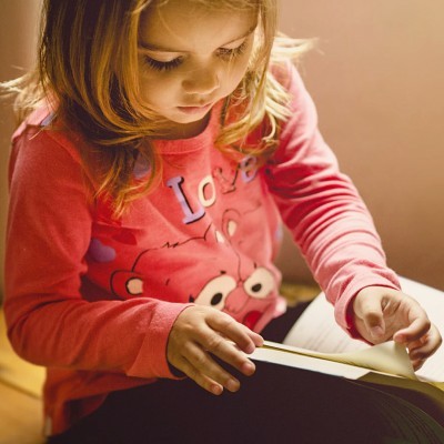 Criança lendo livro com camisola rosa e estampa de urso