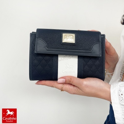 Carteira Cavalinho preto e branco com emblema dourado segurada por mão