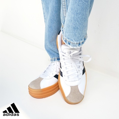 Ténis Adidas brancos com recortes bege e pretos e sola castanha em fundo branco