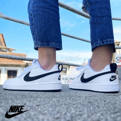 Sapatilhas Nike brancas com detalhes em preto vistas de lado em pessoa com jeans ao ar livre