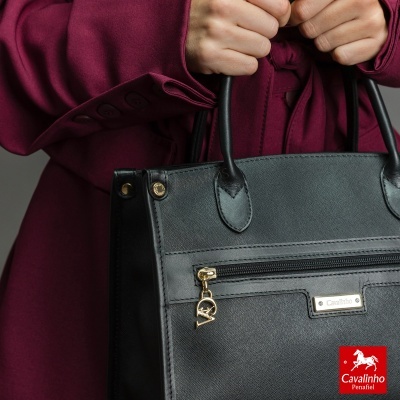 Bolsa preta Cavalinho em mãos com casaco vinho