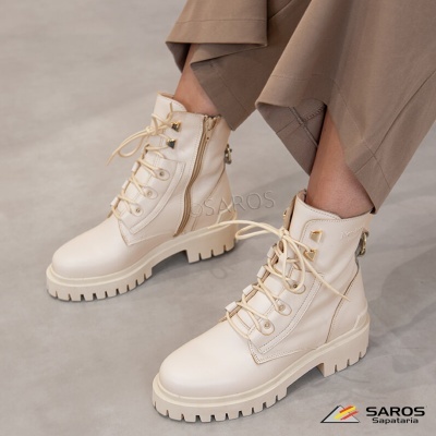 Botas altas bege com sola grossa e atacadores, calças castanhas claras, fundo cinzento.